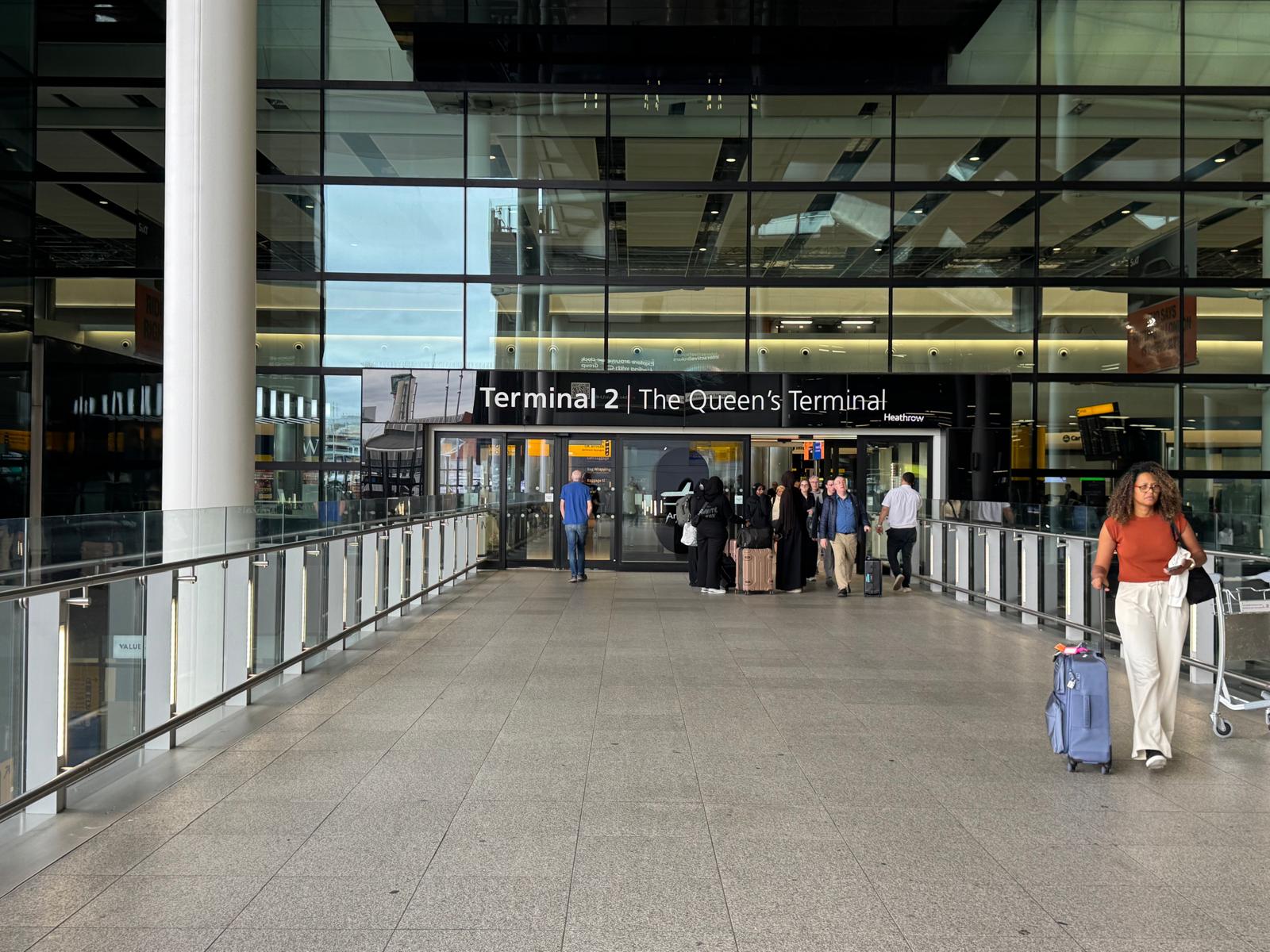 Passengers wheeling suitcases along the walkway from Heathrow Terminal 2 arrivals
